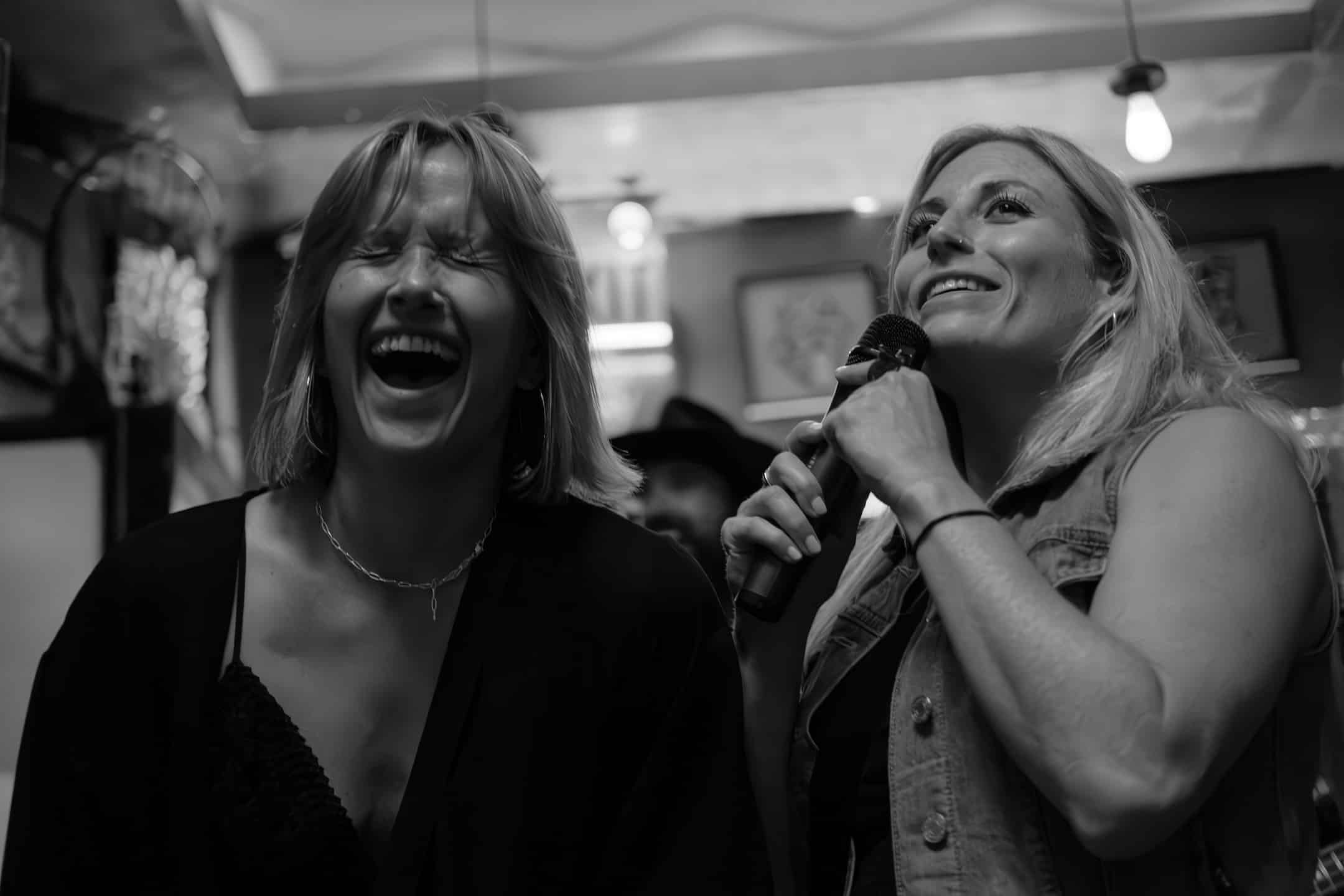 two women laugh as they hold a microphone